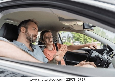 bearded dad pointing while showing direction to teenage son driving car Royalty-Free Stock Photo #2297940919