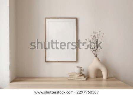 Neutral home still life. Decorative boho interior. Vase with bouquet of dry plants, grass on wooden table. Blank picture frame mockup hanging on wall. White cup of coffee, books. Artistic poster. Royalty-Free Stock Photo #2297960389