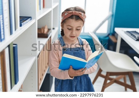 Adorable hispanic girl student reading book at classroom