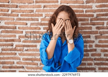 Beautiful brunette woman standing over bricks wall rubbing eyes for fatigue and headache, sleepy and tired expression. vision problem 