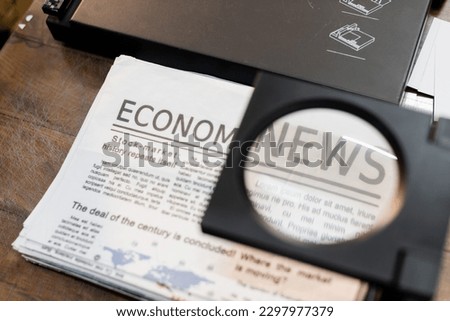 magnifying glass over newspapers with economic news in print center Royalty-Free Stock Photo #2297977379