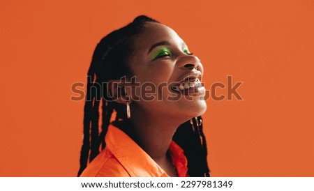 African woman with makeup and face piercings smiling with her eyes closed. Black woman standing against an orange background. Royalty-Free Stock Photo #2297981349