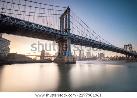 Manhattan Bridge seen from the coast next to the D.U.M.B.O area, during dusk with completely clear skies. Manhattan skyline can be seen on the back