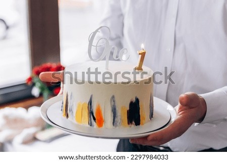 Happy birthday! Close up image man hold first birthday sweet cake surprise number one inscription with burning candle, presents gifts flowers
