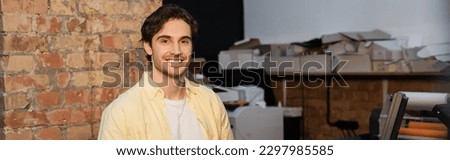happy man in yellow shirt standing and smiling in print center, banner