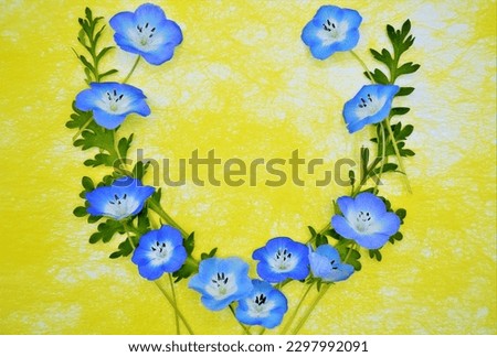 Blue nemophila flowers and leaves circular frame on yellow washi paper background