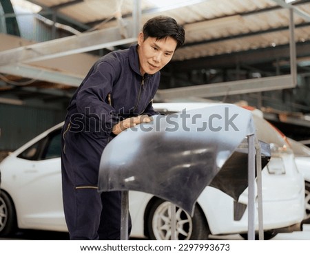 Auto mechanic examining automobile body front bumper before put it on damaged car at auto repair service station. Asian repairman fixing vehicle bumper broken from collision crash accident on road. Royalty-Free Stock Photo #2297993673