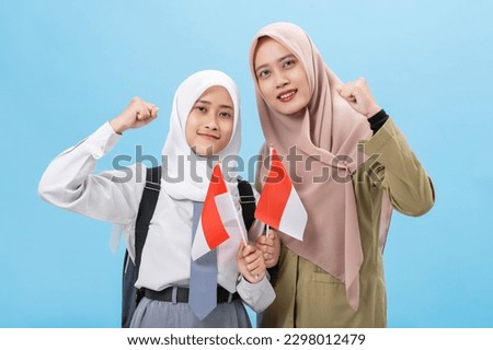 Muslim woman student with a teacher celebrate indonesia independence day waving flag of indonesian isolated over blue background Royalty-Free Stock Photo #2298012479