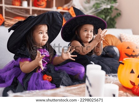 Adorable twin girls having halloween party clapping hands at home
