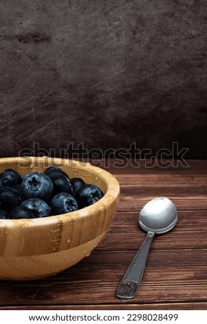 Freshly washed blueberries in a wooden bowl placed on a table. Vertical image with selective focus, water drops as a detail.