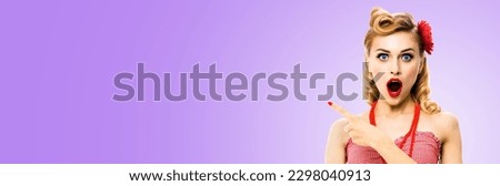 Portrait of shocked beautiful woman with open mouth. Pin up girl show, demonstrate, advertise, point finger aside. Vintage sale ad advertisement concept. Isolated light purple background. Wide image.
