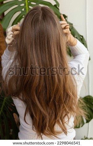 Natural blonde woman fixing her long hair and touching her head in a gently way. Top view, arms raised, hair in movement. Plants in the background. Royalty-Free Stock Photo #2298046541