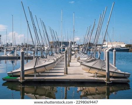 Perspective of a floating dock with covered sailing dinghies used for sailing lessons for beginners on the campus of an urban public university in Florida. For nautical and "back to school" themes. Royalty-Free Stock Photo #2298069447