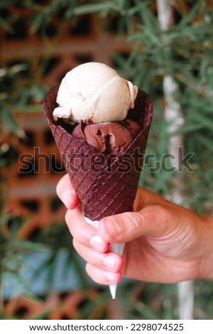 A hand holds a cone with scoops of ice cream. A delicious cold dessert in summer