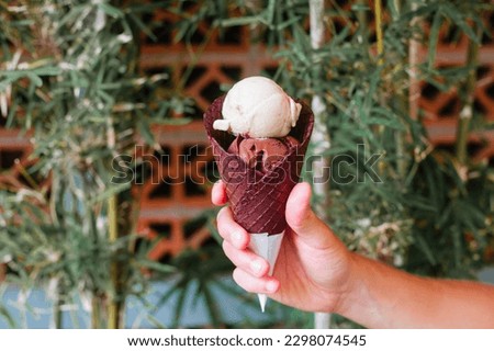 A hand holds a cone with two scoops of ice cream. Natural delicious dessert