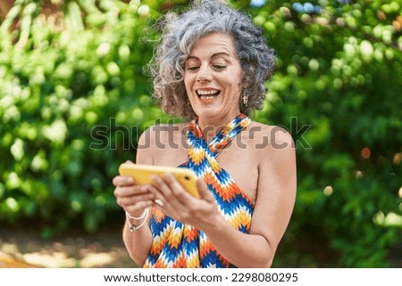 Middle age grey-haired woman smiling confident watching video on smartphone at park