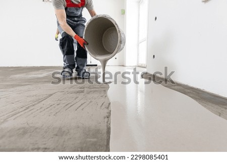 Worker use screed concrete epoxy for level. Leveling with mixture of cement for floors. Royalty-Free Stock Photo #2298085401