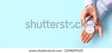 Hands of man holding box with engagement ring on light blue background with space for text Royalty-Free Stock Photo #2298099569