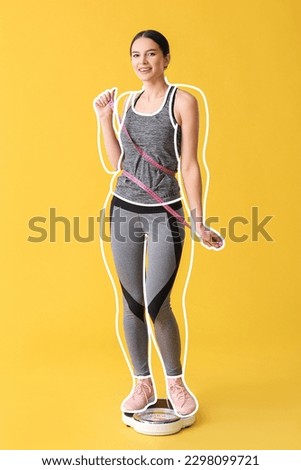 Happy young woman after slimming measuring her waist while standing on scales against yellow background