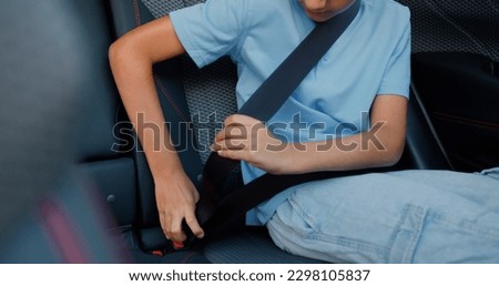 Portrait of likable satisfied teen boy which sitting in car's backseat and fastens safety belt before trip Royalty-Free Stock Photo #2298105837
