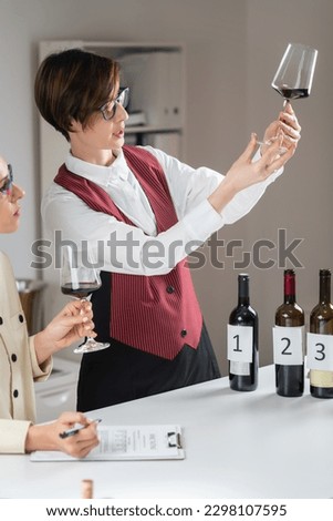 Sommelier holds a wineglass and evaluates the appearance of a red wine, looking at its color, clarity, and viscosity. Royalty-Free Stock Photo #2298107595