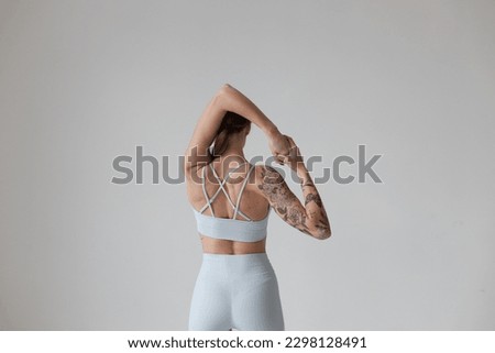 Young girl with brown hair, with a tattoo in a gray top and shorts on a white background with headphones. Sports, fitness, stretching and yoga, meditation