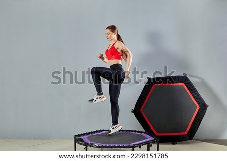 A young athletic girl does a rebound exercise. Fitness trainer in sportswear jumps on a sports trampoline gym. Royalty-Free Stock Photo #2298151785