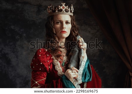 medieval queen in red dress with handkerchief and crown on dark gray background. Royalty-Free Stock Photo #2298169675
