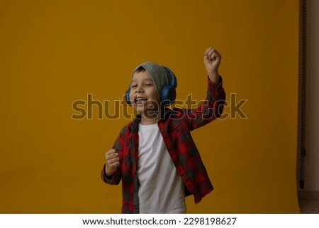 funny boy with headphones. lucky boy. the child laughs. listen to music with headphones. the child is dancing. yellow background. white T-shirt.