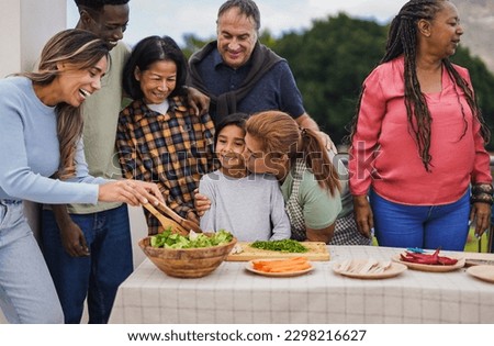 Multi generational people cooking at house terrace rooftop - Multiracial friends preparing food with  female child outdoor during weekend day - Grandmother having tender moment with granddaughter Royalty-Free Stock Photo #2298216627