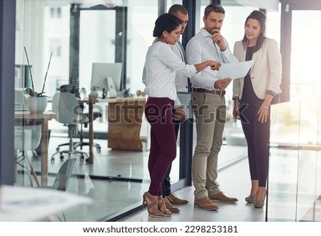 Finding business solutions as a team. a group of coworkers talking over some paperwork in an office. Royalty-Free Stock Photo #2298253181