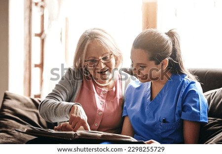 I have so many stories in here. a nurse and a senior woman looking at a photo album together. Royalty-Free Stock Photo #2298255729