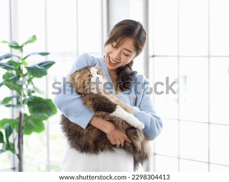 Millennial Asian young female owner standing smiling holding showing love playing with cute fat tabby long hair little domestic kitty furry purebred pussycat pet friend in arms in living room at home. Royalty-Free Stock Photo #2298304413