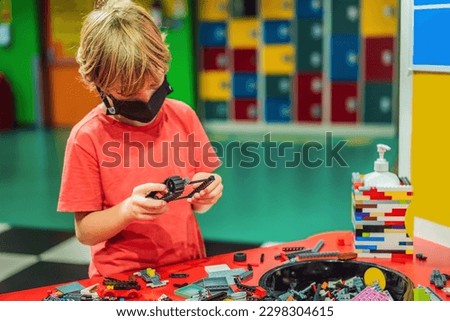 A boy in a medical mask plays with a constructor. child playing and building with colorful plastic bricks table. Early learning and development
