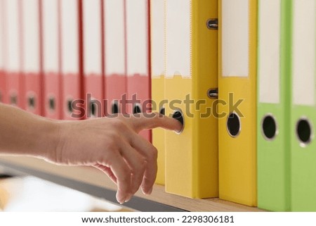 Hand of secretary taking yellow ring binder with documents. Organized structure of colorful folders with archive files put in row on shelf Royalty-Free Stock Photo #2298306181