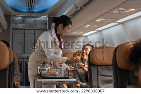 Air hostess or cabin crew working in airplane. Female flight attendant serving orange juice to businesswoman passenger on board. Airline transportation and tourism concept. Royalty-Free Stock Photo #2298338307