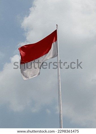 the red and white flag of Indonesia flutters in the wind in a clear sky