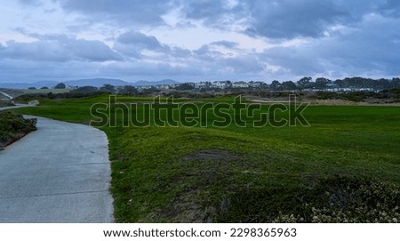 Coastal trail and green grass field with cloudy sky.