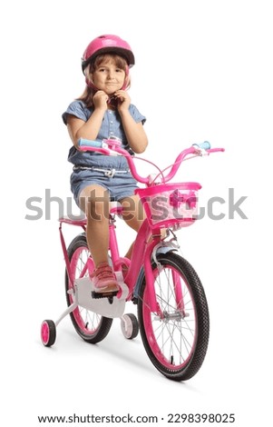 Girl putting on a helmet and sitting on a bicycle with training wheels isolated on white background