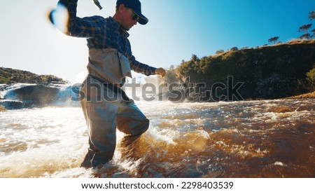 Fly fishing in a rapid river. Fisherman in waders slowly walks from the furious murky river Royalty-Free Stock Photo #2298403539