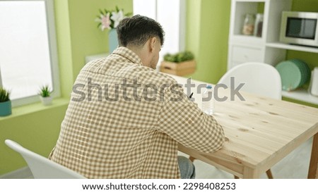 Young arab man writing on document sitting on table at home