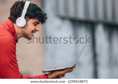 young man on the street with headphones and laptop Royalty-Free Stock Photo #2298418873