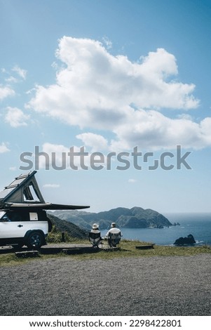 Couple sitting in a camping chair in nature with a view of Island in a beautiful blue sky with an overlanding car with a rooftop tent and an awning. Royalty-Free Stock Photo #2298422801