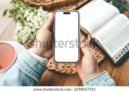 Phone in hands with an isolated screen and an open bible, space for your text.