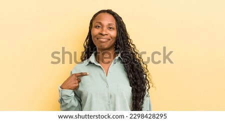 black pretty woman looking proud, confident and happy, smiling and pointing to self or making number one sign
