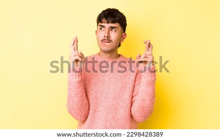 young adult hispanic man crossing fingers anxiously and hoping for good luck with a worried look