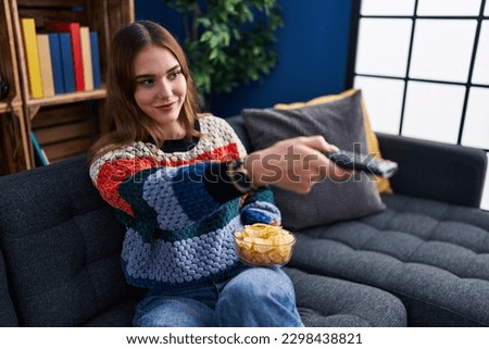 Young woman watching movie sitting on sofa at home Royalty-Free Stock Photo #2298438821