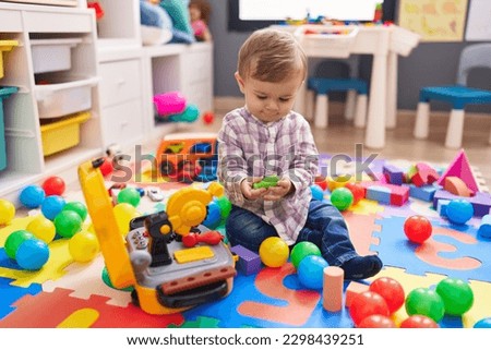 Adorable caucasian boy playing with balls sitting on floor at kindergarten