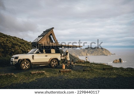 Couple sitting in a camping chair in nature with a view of Island in a beautiful blue sky with an overlanding car with a rooftop tent and an awning. Royalty-Free Stock Photo #2298440117