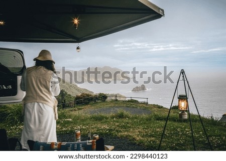Couple sitting in a camping chair in nature with a view of Island in a beautiful blue sky with an overlanding car with a rooftop tent and an awning. Royalty-Free Stock Photo #2298440123